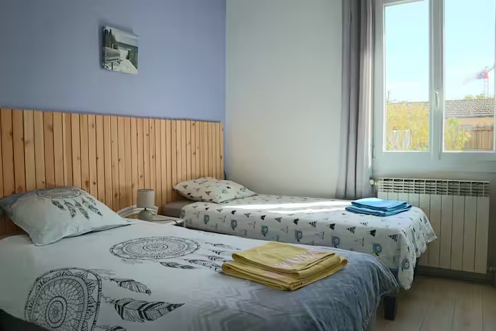 Chambre au mur mauve, lits faits avec draps et serviettes
