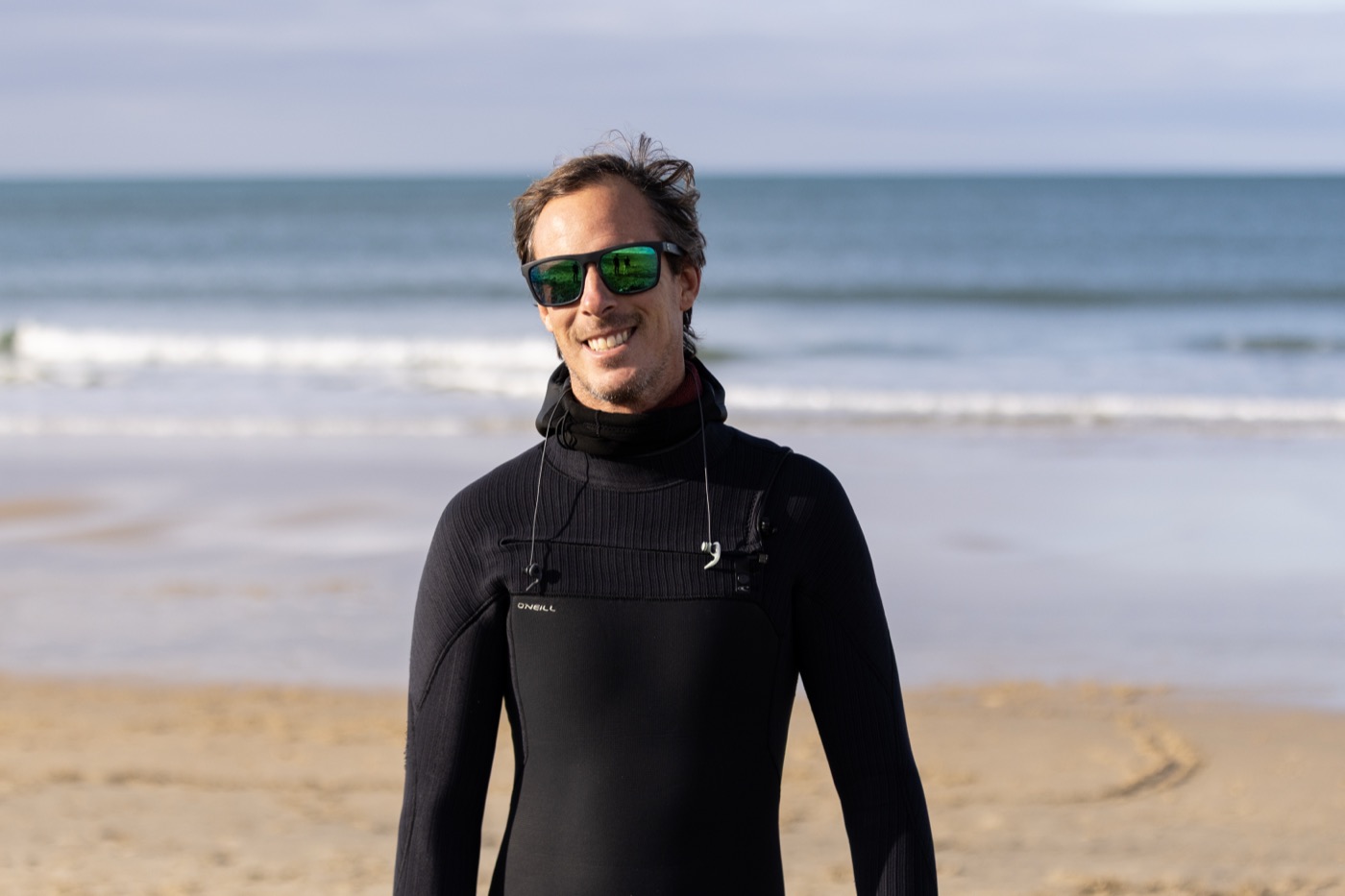 Portrait de Sylvain en combinaison sur la plage, sourire et lunettes de soleil